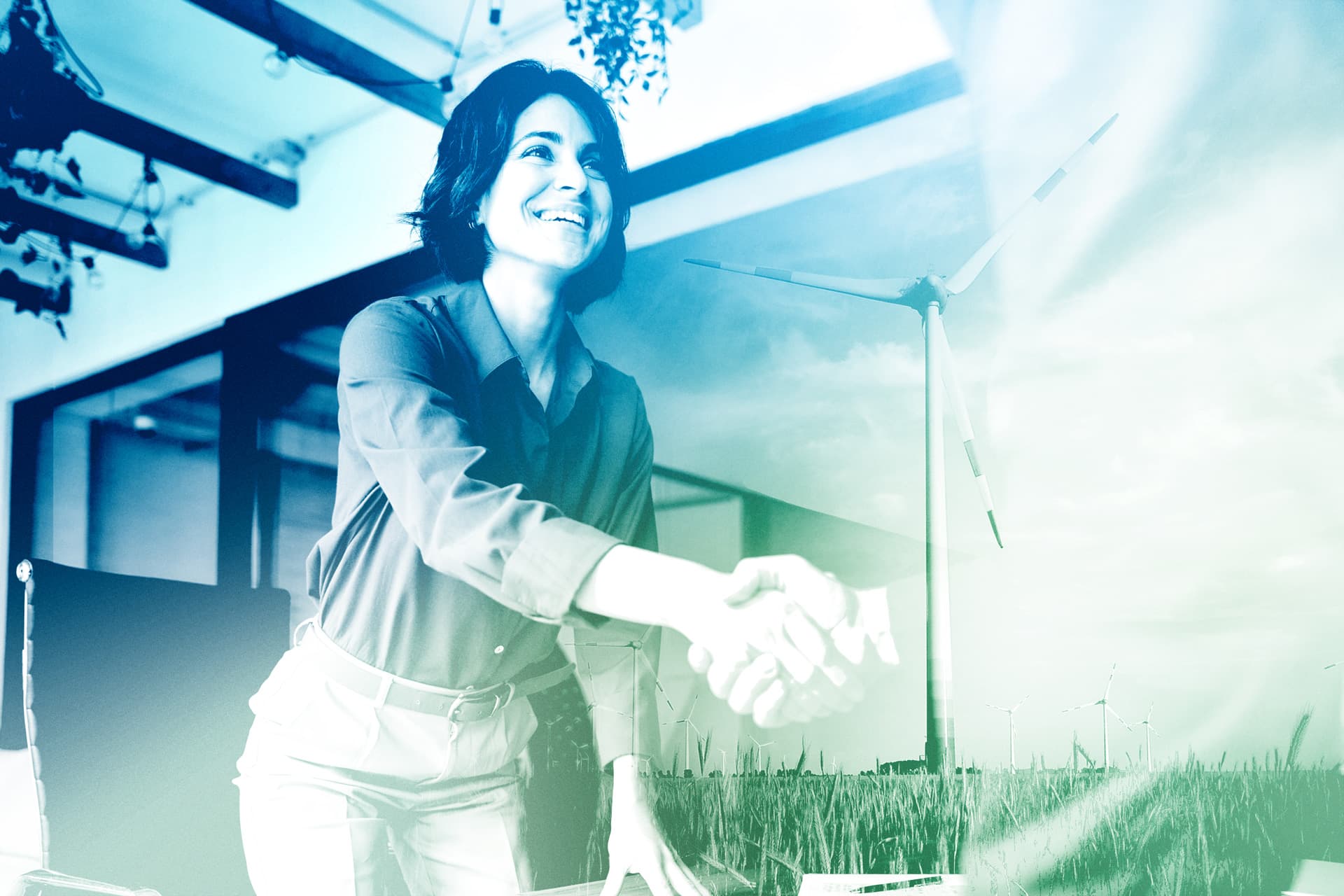 Eine Person schüttelt in einem modernen Büro die Hand, mit einem Windrad im Hintergrund, symbolisiert nachhaltige Investitionen.